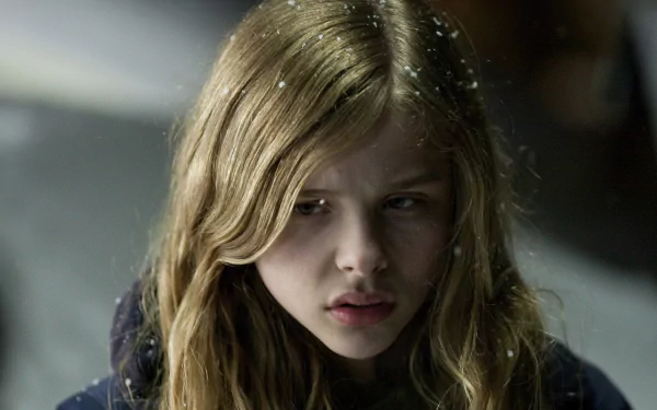 HD desktop wallpaper from the movie Let Me In, featuring a close-up of a young girl with long blonde hair and a serious expression in a dimly lit setting.
