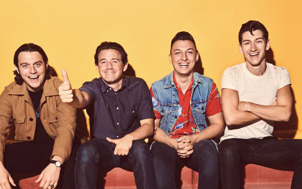 A vibrant HD wallpaper featuring the Arctic Monkeys rock band, showcasing four members smiling and posing against a bright yellow background, capturing their energetic style.
