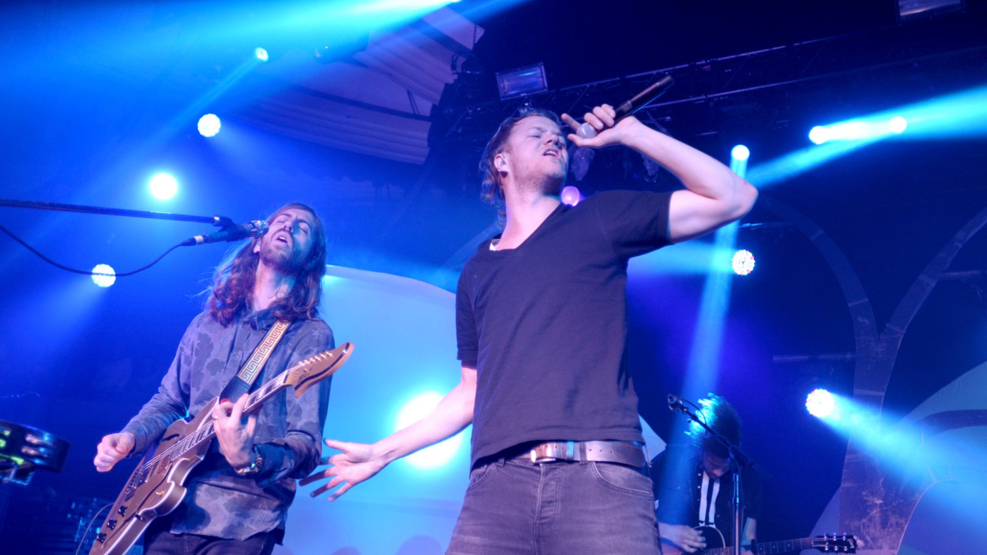 HD desktop wallpaper of American alternative band Imagine Dragons performing live under blue stage lights.