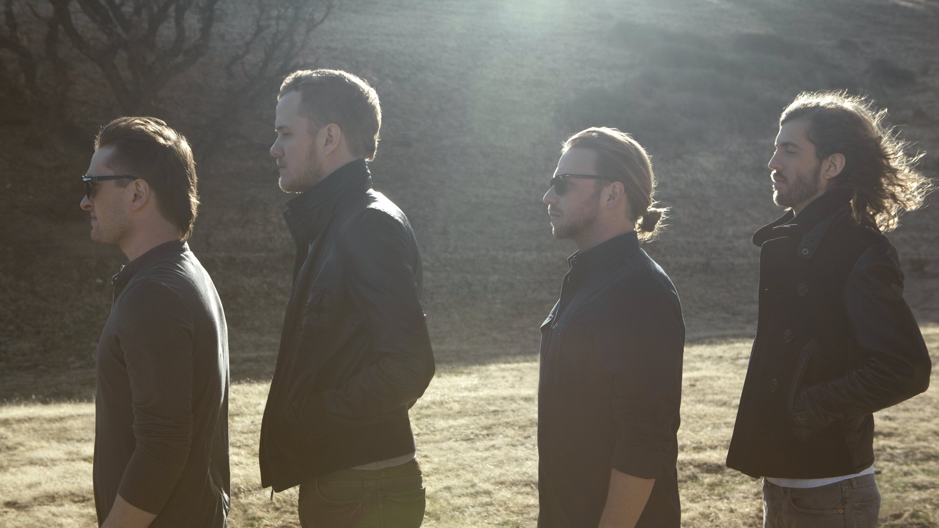 A 4K Ultra HD background featuring the American alternative band Imagine Dragons, showcasing the members standing in a line against a sunlit landscape.