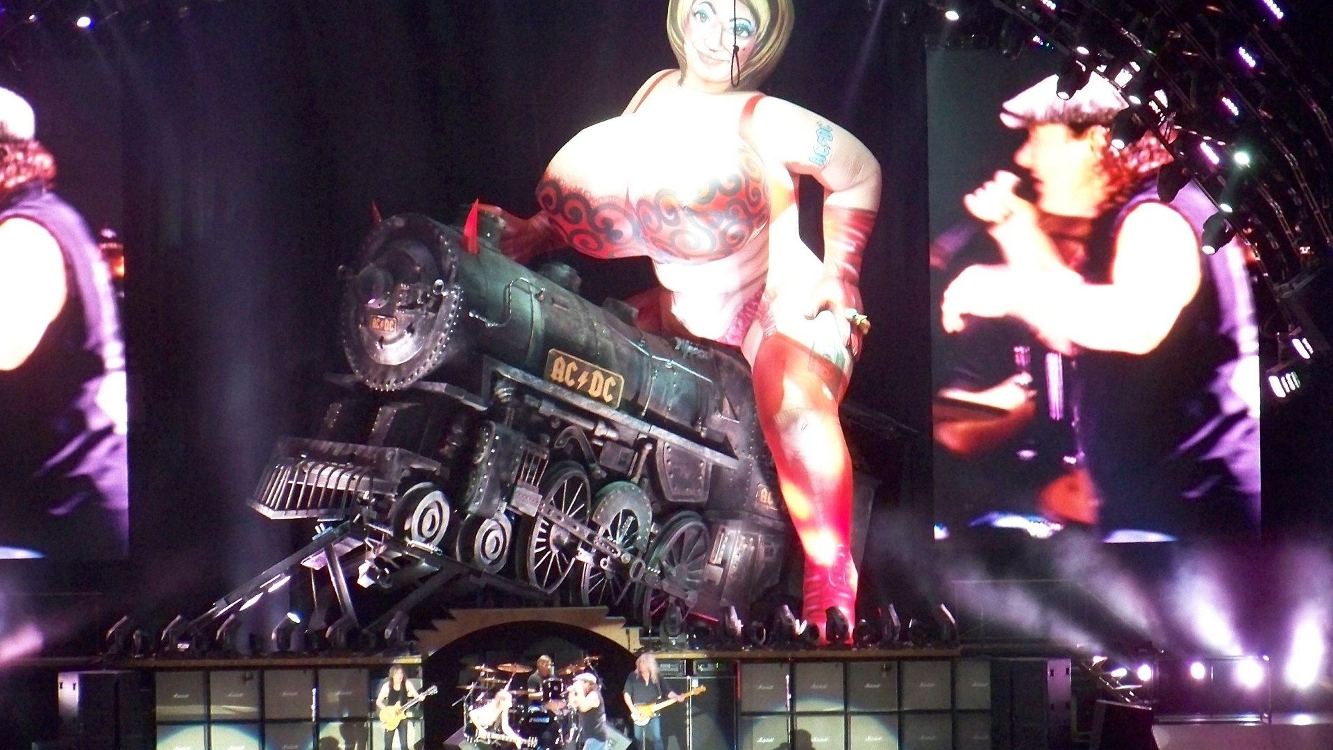 2K Quad HD PC desktop wallpaper: AC/DC concert stage with a roaring locomotive prop, giant inflatable figure and live band on massive screens.