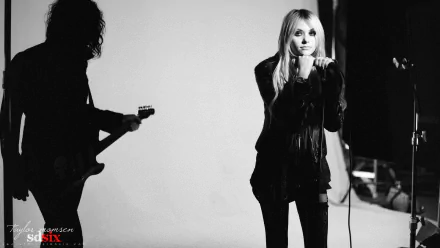 Black-and-white HD PC desktop wallpaper of a female rock singer at a microphone, with a guitarist silhouetted to the left in a high-contrast studio shot.