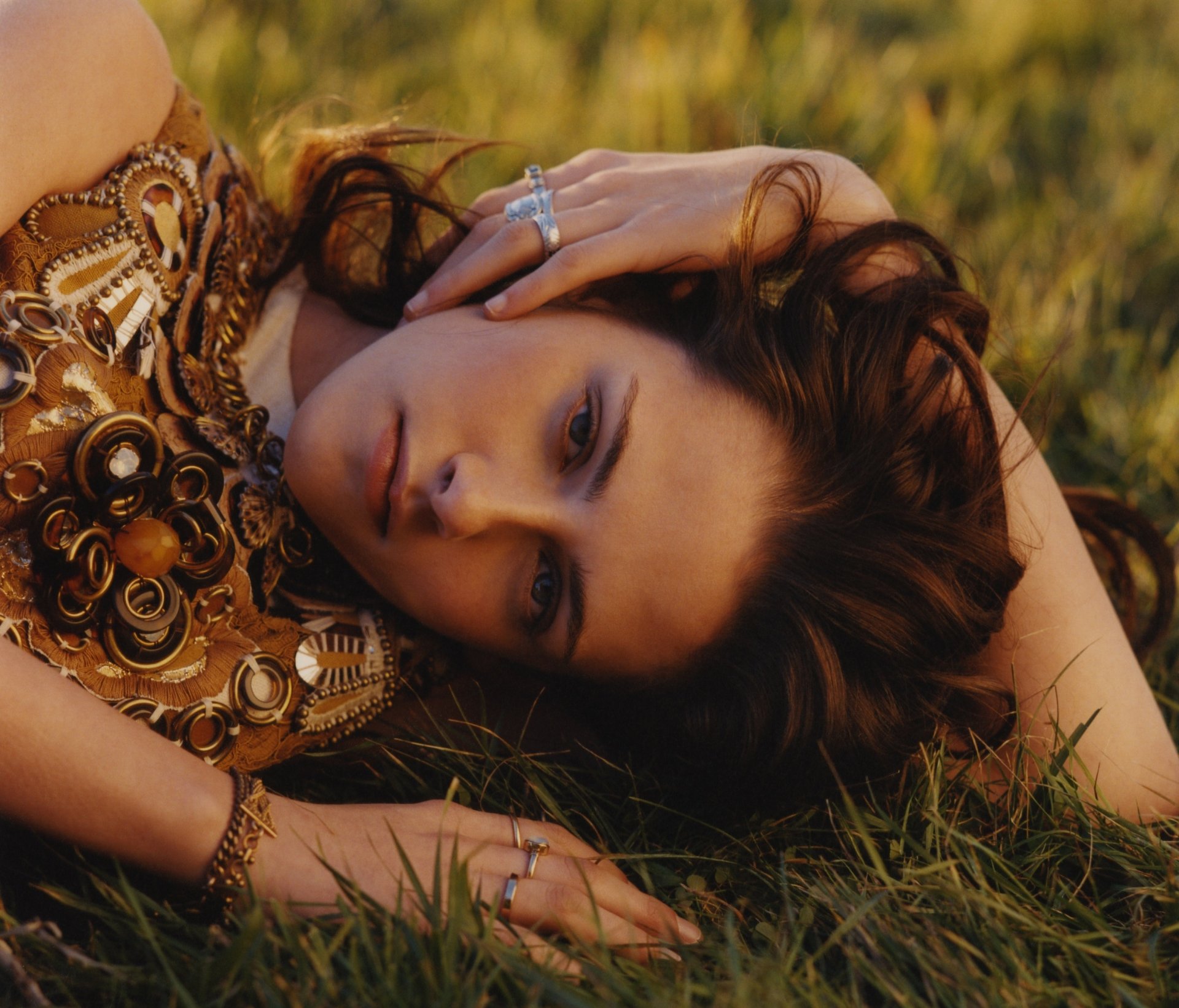 HD desktop wallpaper featuring Kristen Stewart, captured in a serene pose on grass, showcasing her intricate outfit and expressive gaze.