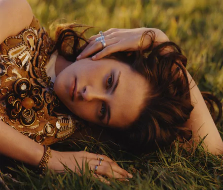 HD desktop wallpaper featuring Kristen Stewart, captured in a serene pose on grass, showcasing her intricate outfit and expressive gaze.
