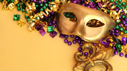 HD desktop wallpaper featuring a gold Mardi Gras mask surrounded by purple, green, and gold beads and festive holiday decorations on a yellow background.