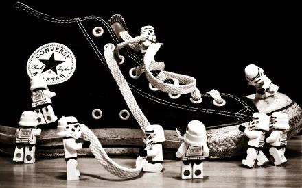 A monochrome HD wallpaper featuring LEGO stormtroopers interacting with a Converse shoe, playfully entwining shoelaces, blending Star Wars flair with creativity.