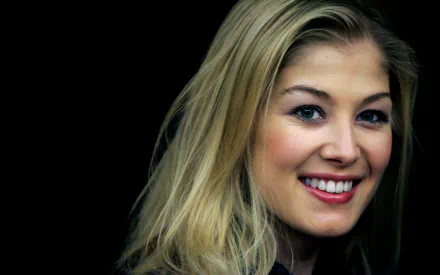 Rosamund Pike smiles in a high-definition wallpaper with a dark background.