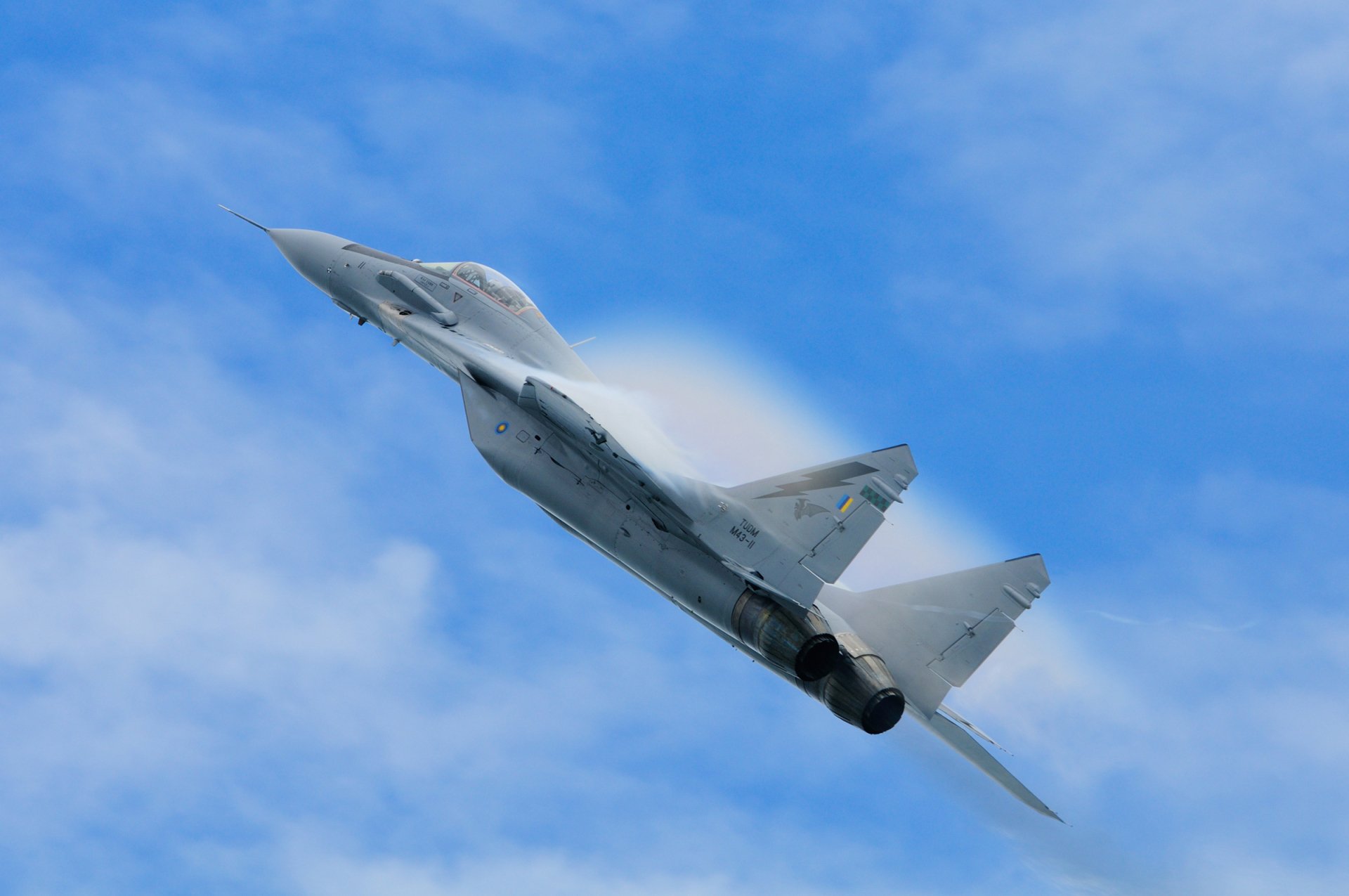 HD desktop wallpaper featuring a Mikoyan MiG-29 military jet soaring through a clear blue sky with visible vapor cones.