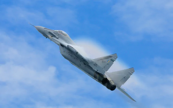 HD desktop wallpaper featuring a Mikoyan MiG-29 military jet soaring through a clear blue sky with visible vapor cones.