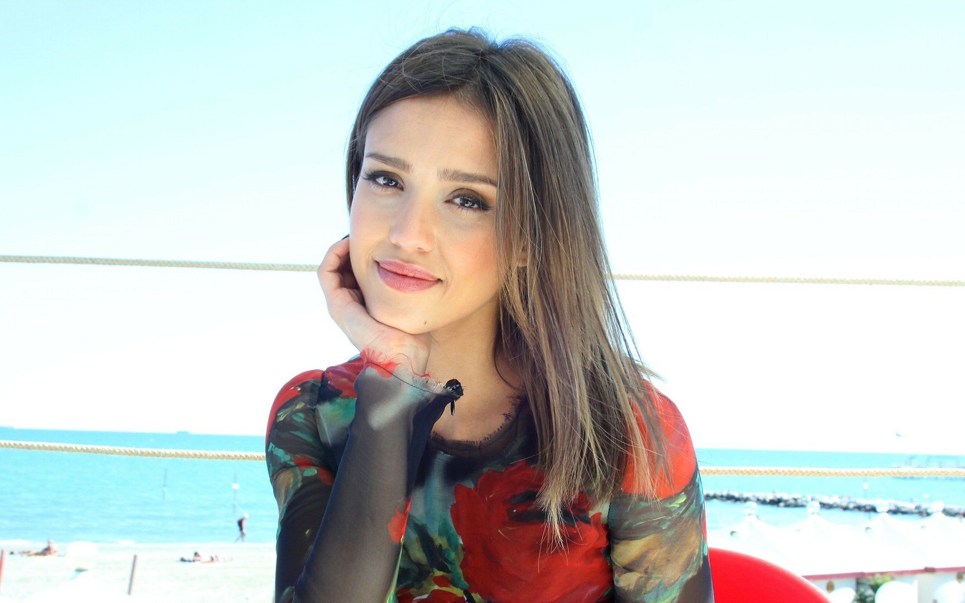 HD desktop wallpaper featuring actress and celebrity Jessica Alba smiling with a blurred seaside background.