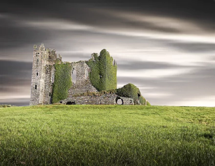 Ballycarbery Castle ruins, a man-made ivy-covered stone keep on a green field beneath dramatic clouds — HD PC desktop wallpaper/background.