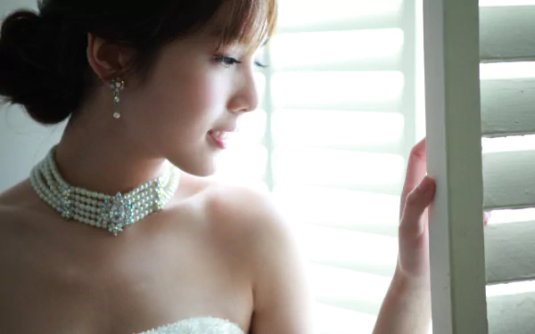HD desktop wallpaper featuring an Asian woman named Catherine wearing elegant earrings and a pearl necklace, gazing thoughtfully out of white blinds.