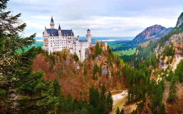 4K Ultra HD PC desktop wallpaper showing the man-made Neuschwanstein Castle perched on a forested Bavarian ridge, flanked by rocky peaks and a sweeping valley under a cloudy sky.