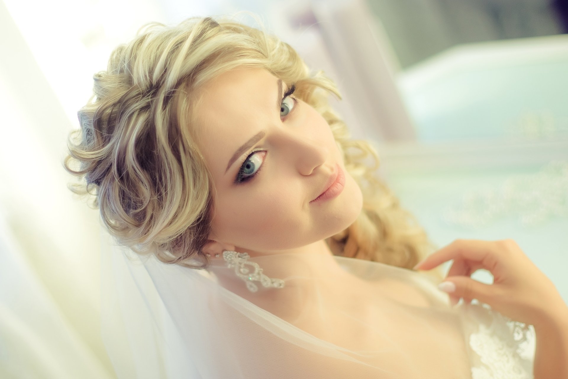 A smiling blonde bride with curly hair and delicate earrings gazes into the distance. This HD desktop wallpaper captures her serene expression and soft features in a luminous setting.