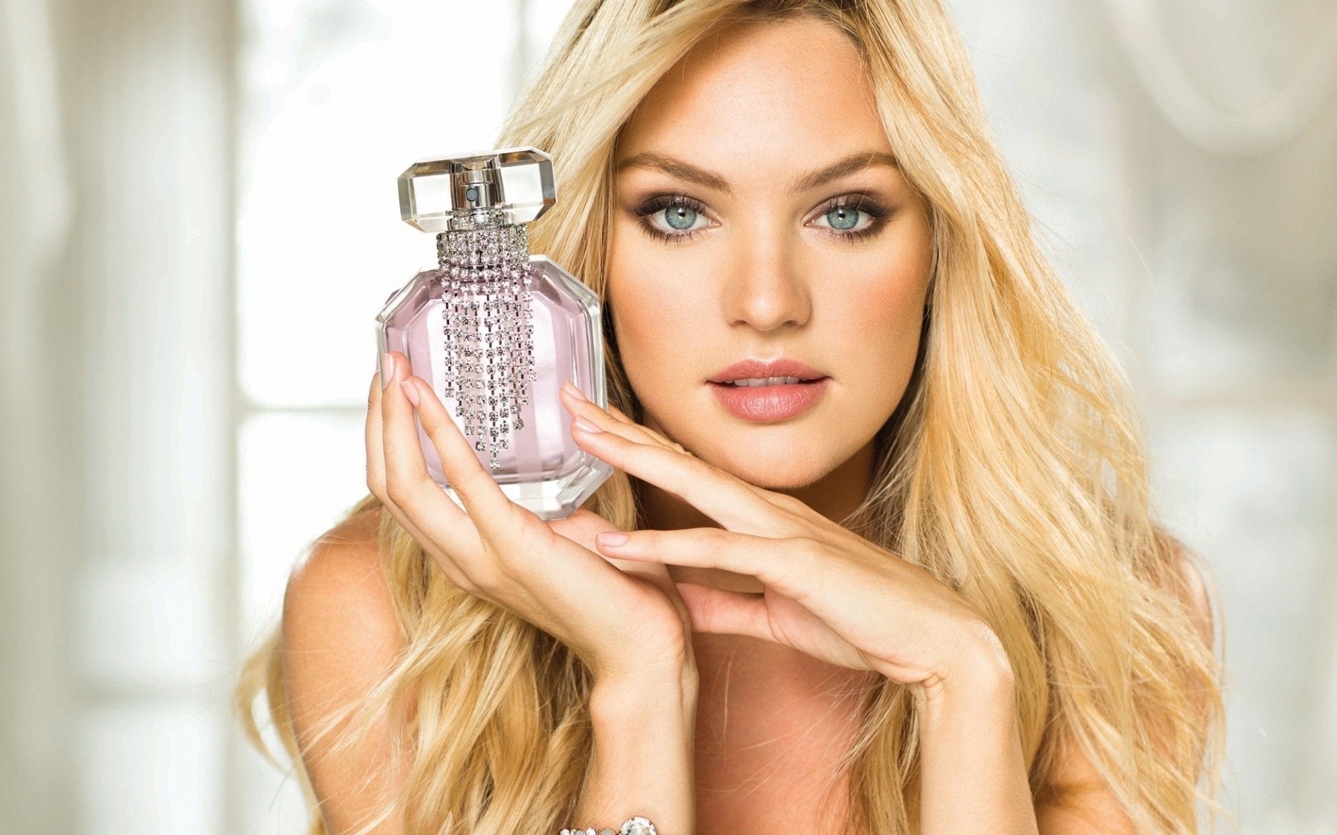 Blonde woman holding a jeweled perfume bottle in a soft-lit close-up — HD PC desktop wallpaper/background.