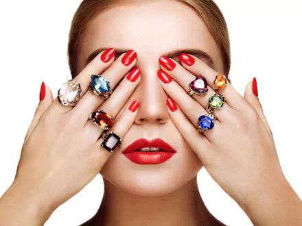 A woman with striking red lips and nails covers her face with hands adorned in vibrant gemstone rings, capturing elegance and style in this 4K Ultra HD portrait.