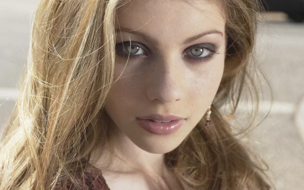 A striking HD desktop wallpaper featuring Michelle Trachtenberg, showcasing her captivating gaze and flowing hair against a blurred outdoor background.