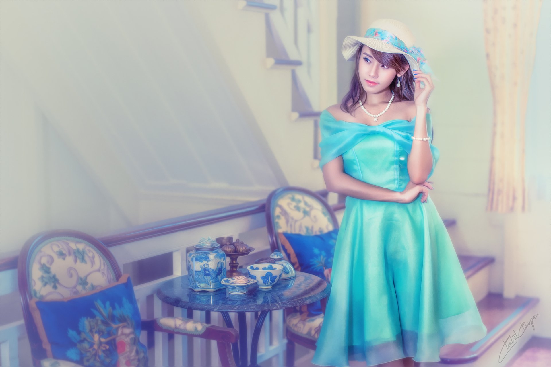 Asian woman in a turquoise dress and Thai hat stands in an oriental room with vintage chairs and a tea set, captured in HD for a PC desktop wallpaper.
