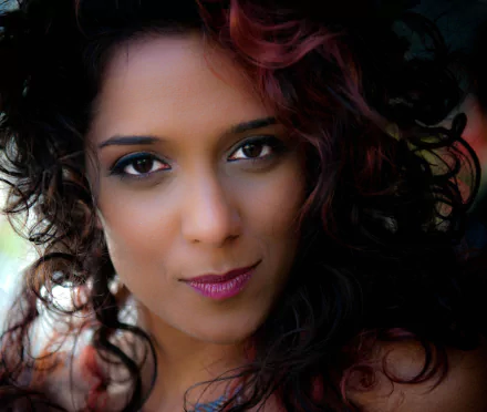 Close-up portrait of a woman's face with curly hair and expressive eyes, 2K Quad HD PC desktop wallpaper background.