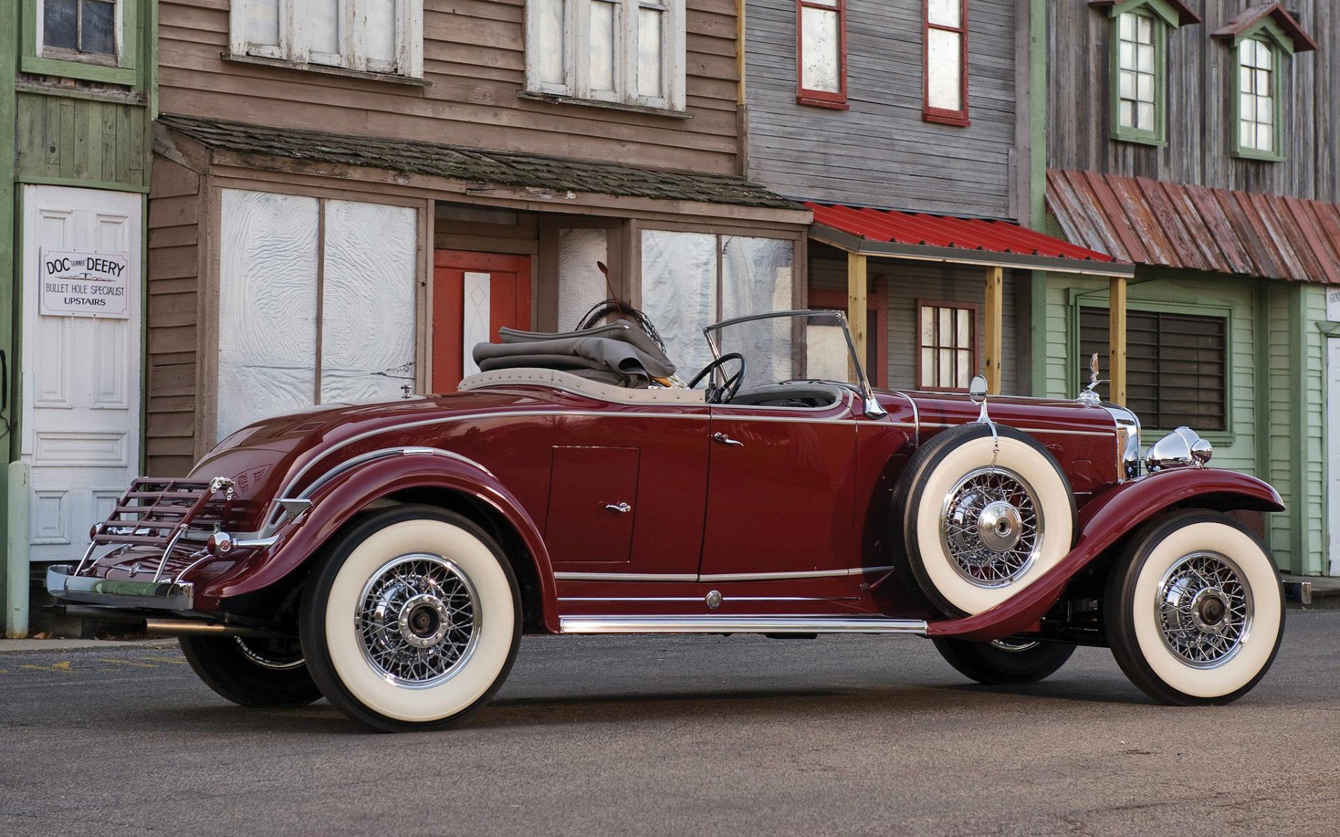 HD desktop wallpaper featuring a maroon 1931 Cadillac convertible parked in front of vintage wooden buildings.