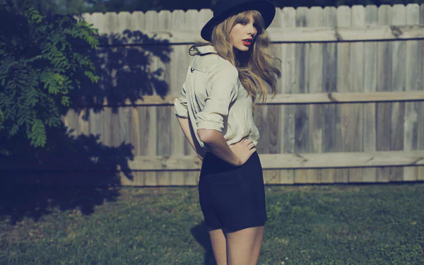 Blonde singer Taylor Swift poses confidently in a stylish outfit and hat against a rustic backdrop, capturing her vibrant music spirit in this HD wallpaper.