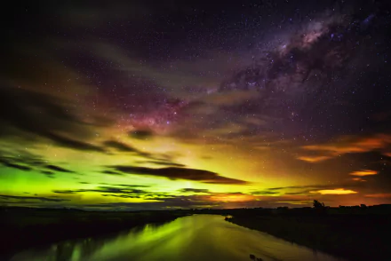 A stunning display of the aurora australis fills the sky over New Zealand, showcasing vibrant green and purple hues reflecting in the water below, with stars twinkling above.