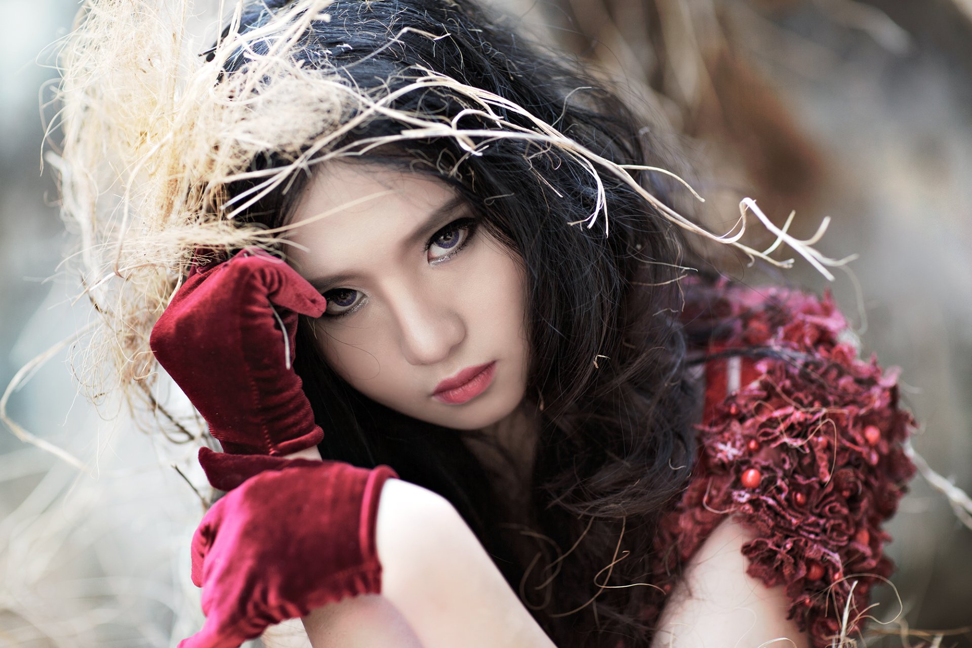 A Vietnamese model with flowing dark hair, wearing red gloves, poses with an intense gaze. This HD desktop wallpaper captures her striking beauty against a blurred, natural background.