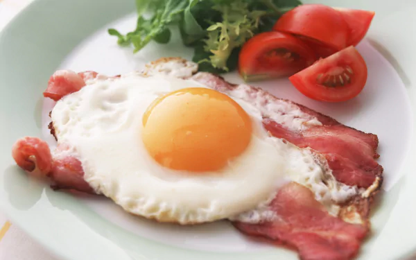 Close-up 4K Ultra HD desktop wallpaper of a sunny-side-up egg served on crispy bacon with fresh tomato slices and greens on a white plate.