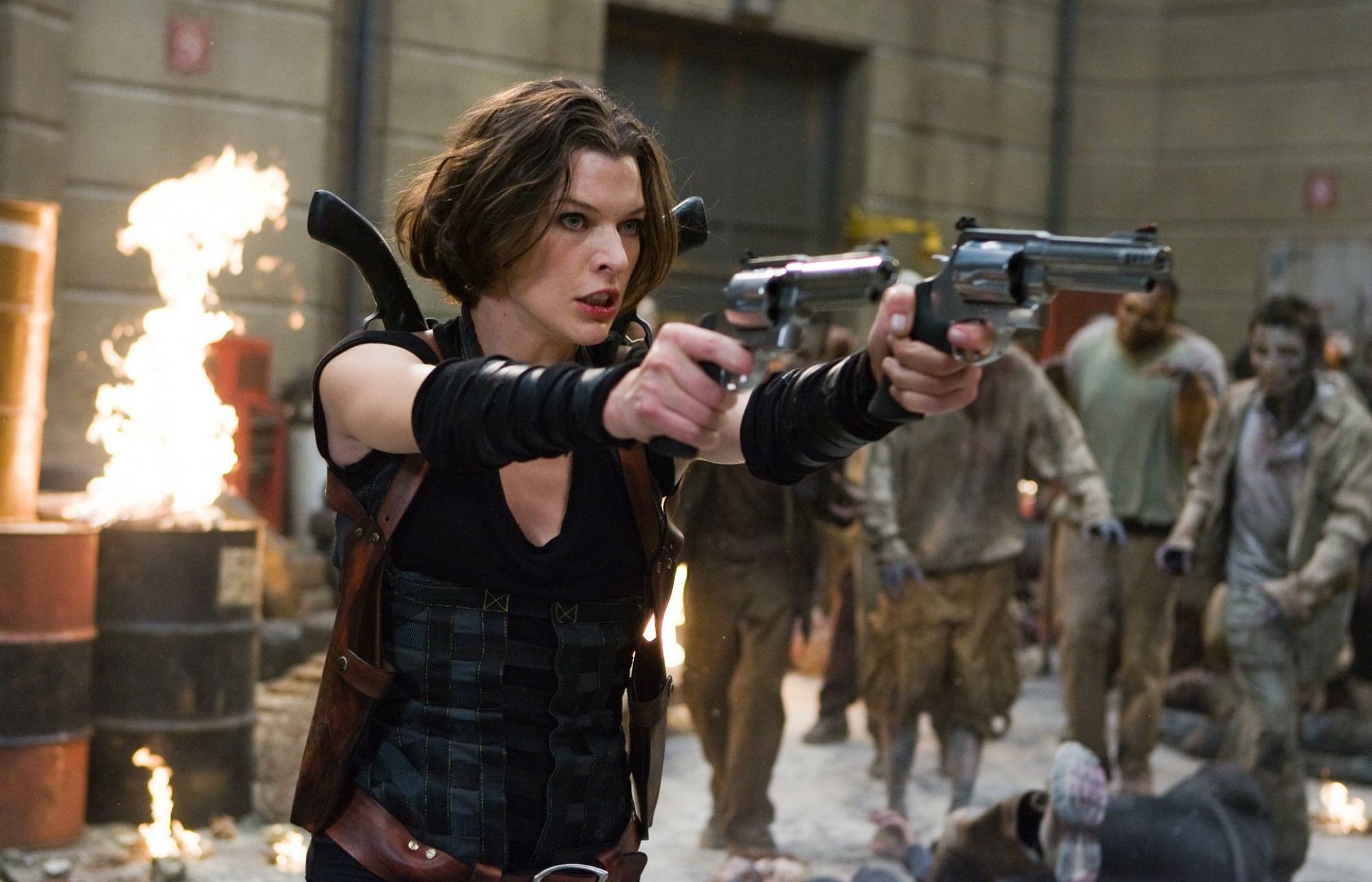Milla Jovovich wields dual handguns in a tense scene from *Resident Evil: Afterlife*, surrounded by flames and zombie adversaries, showcased in this HD desktop wallpaper.
