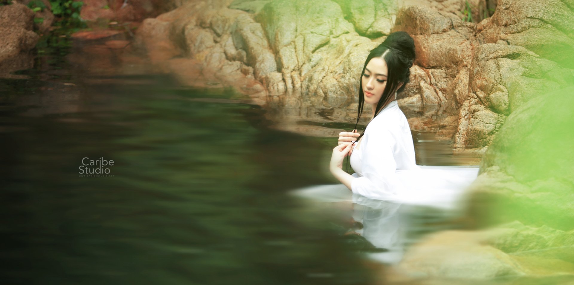 A Vietnamese woman in traditional attire immerses in calm water surrounded by natural rock formations, captured in an HD Asian-themed desktop wallpaper.