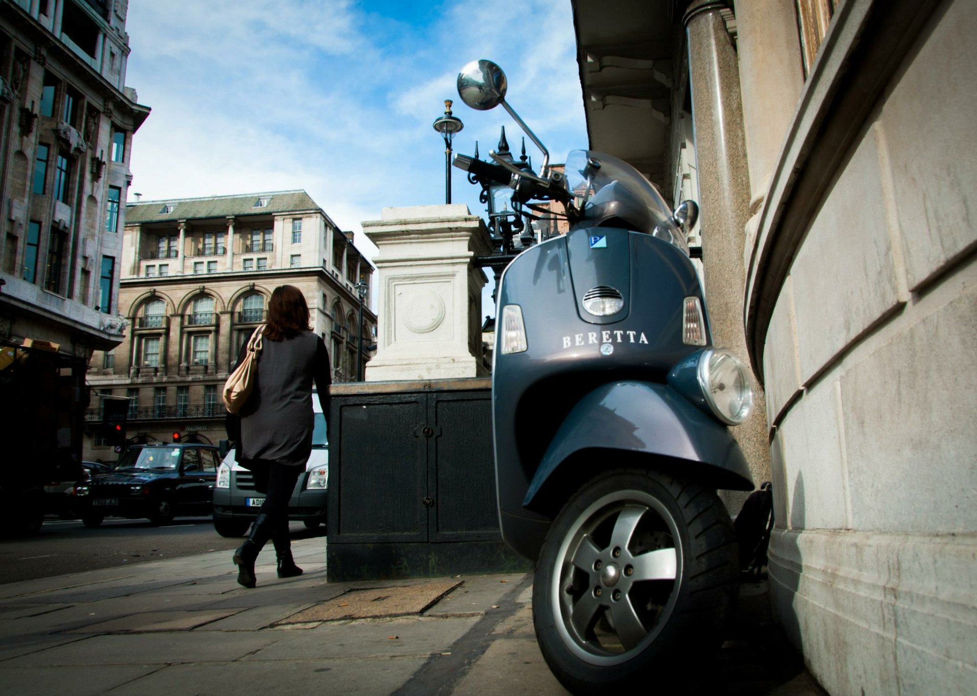 Blue Vespa scooter parked on a London, England, United Kingdom sidewalk amid man-made historic buildings; pedestrian passes by — HD PC desktop wallpaper background.