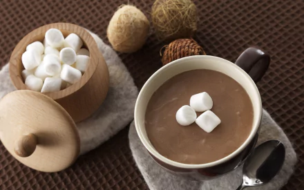 HD desktop wallpaper of a cup of hot chocolate topped with marshmallows, accompanied by a wooden bowl filled with marshmallows on a textured brown surface.