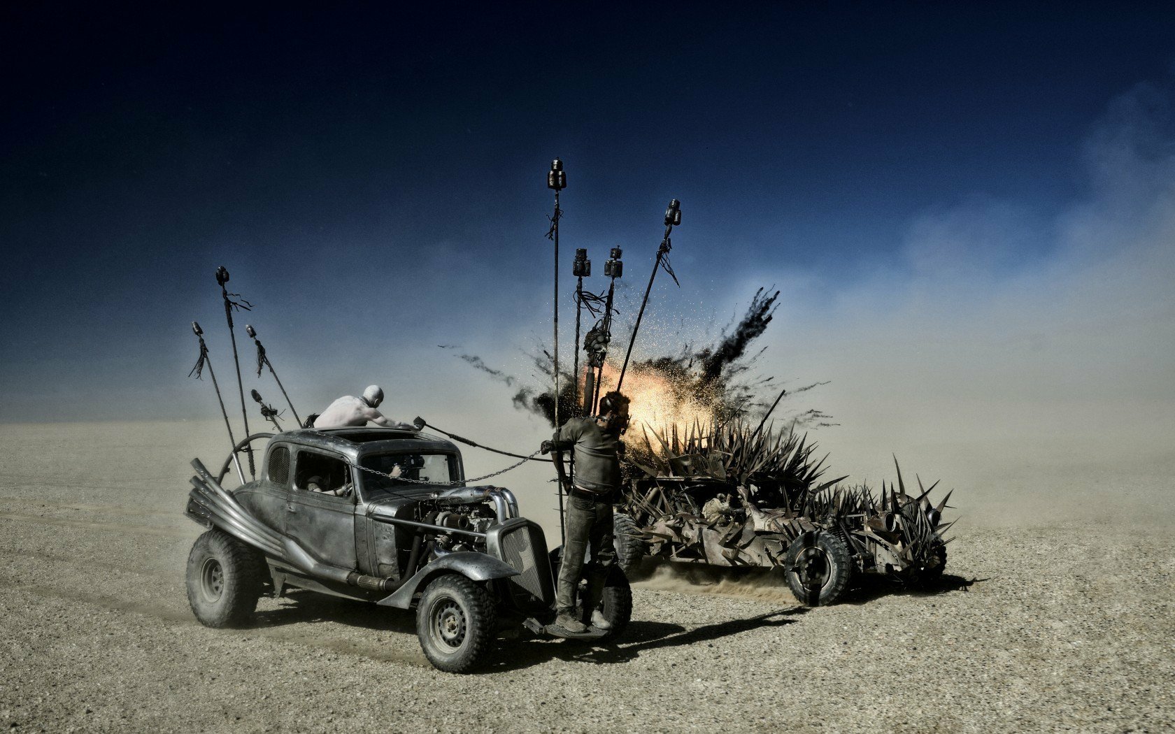 HD desktop wallpaper featuring Max Rockatansky, played by Tom Hardy, in a scene from the movie Mad Max: Fury Road with armored vehicles in a desert setting.