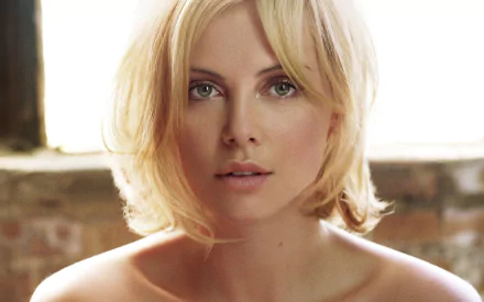 HD PC desktop wallpaper featuring a close-up portrait of celebrity Charlize Theron with blonde hair and a neutral expression against a soft, blurred background.