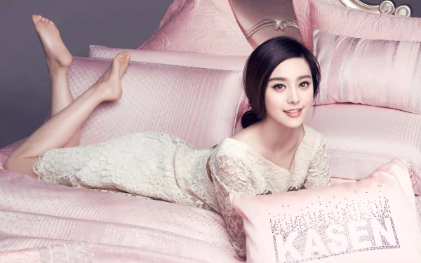 A serene image of actress Fan Bingbing, elegantly posed on a pile of soft pink pillows, showcasing her warm smile against a luxurious backdrop. An elegant HD desktop wallpaper.