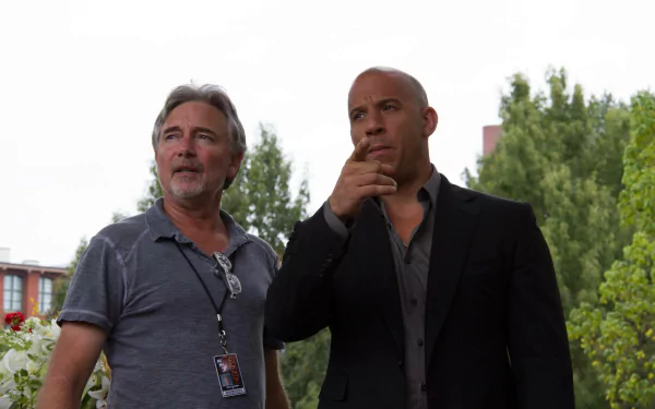 Vin Diesel on set with a crew member during the filming of Furious 7, captured in a high-definition desktop wallpaper, showcasing their focus amidst a vibrant background.