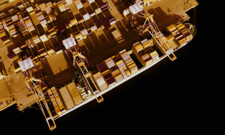 An aerial view of a container ship loaded with colorful shipping containers, set against a dark background, showcasing its massive structure and industrial design.
