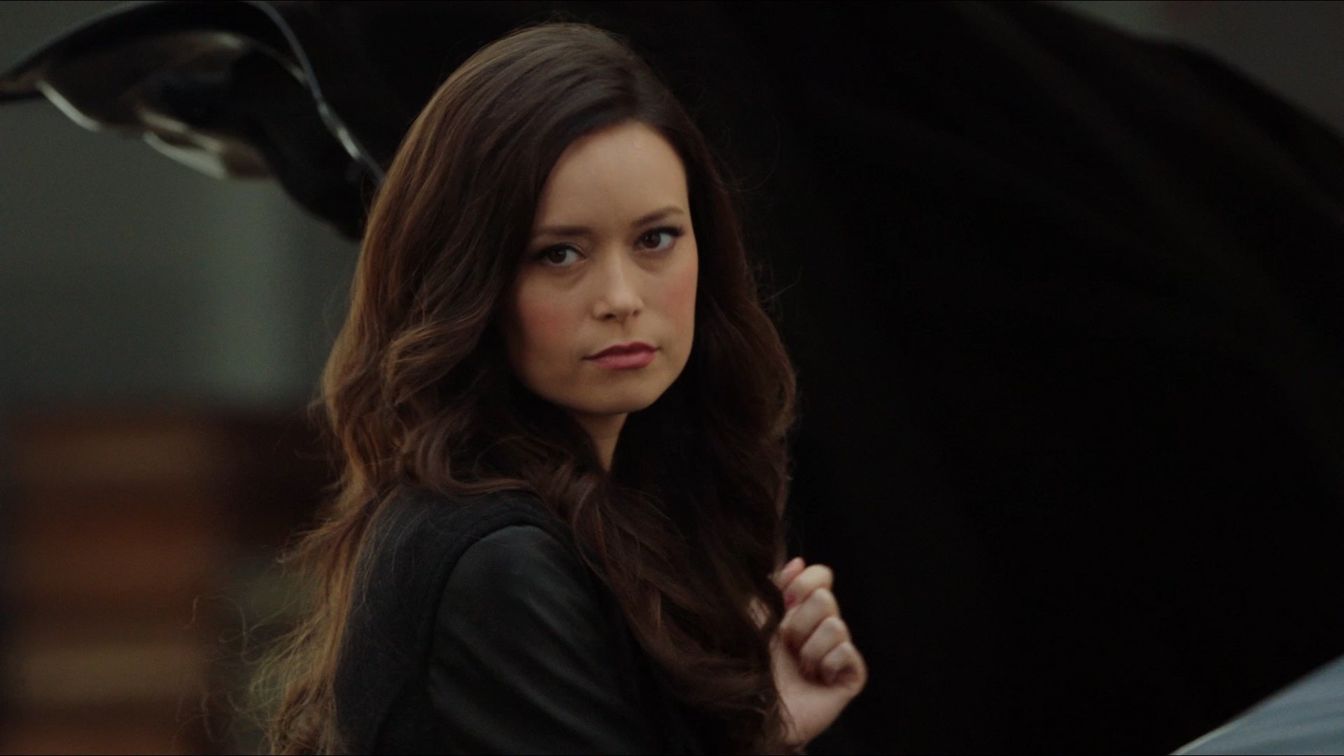 HD desktop wallpaper featuring celebrity Summer Glau with long brown hair, wearing a dark outfit and a serious expression against a blurred background.