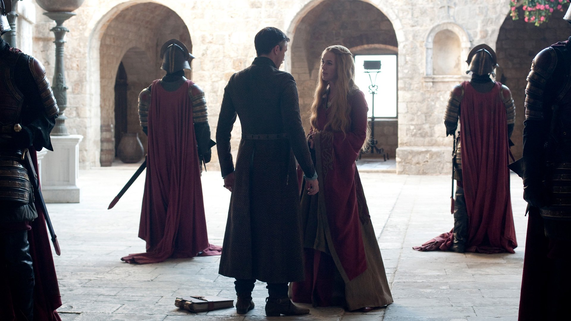 Aidan Gillen as Petyr Baelish and Lena Headey as Cersei Lannister in a scene from the TV show Game of Thrones, set in a medieval courtyard.