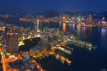 Nighttime cityscape of Hong Kong's Victoria Harbour, with illuminated skyscrapers and waterfront structures reflecting on the water, captured in high-definition detail.