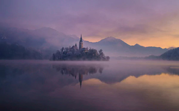 HD wallpaper of the Assumption of Mary Church on a misty island, surrounded by calm water and mountains under a colorful twilight sky.