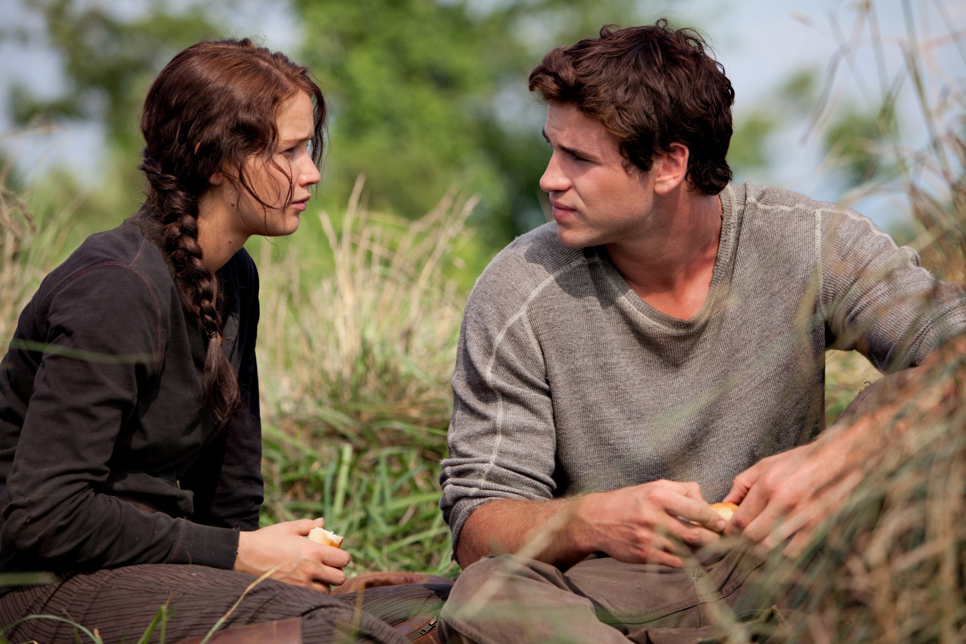 HD PC desktop wallpaper from The Hunger Games movie featuring Katniss Everdeen and Peeta Mellark sitting and talking in a natural, outdoor setting.
