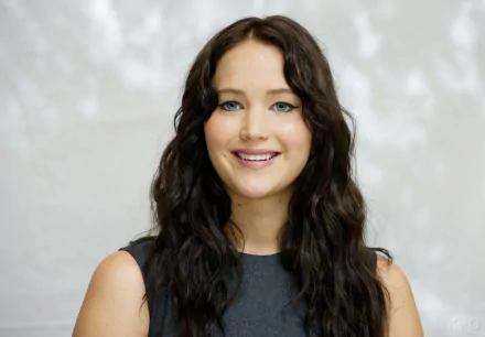 A close-up of Jennifer Lawrence smiling, featuring her long, wavy hair and wearing a simple black outfit, set against a soft, blurred background. This image serves as an HD desktop wallpaper.