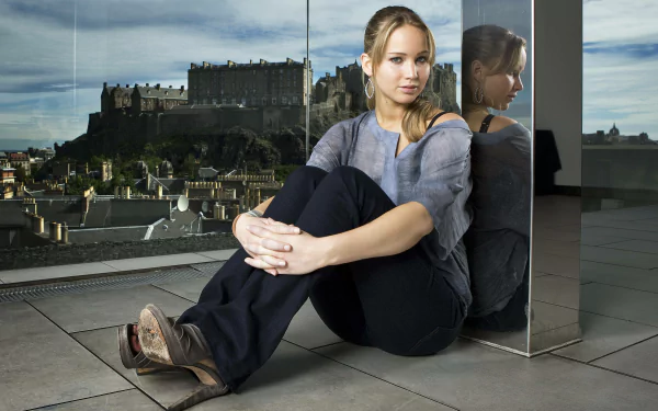 A 4K Ultra HD wallpaper featuring Jennifer Lawrence seated against a glass panel, with a view of a castle in the background and a reflective surface beside her.