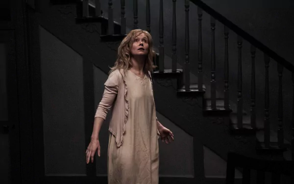 HD PC desktop wallpaper featuring Essie Davis in a scene from the movie The Babadook, standing near a dark staircase with a tense expression.