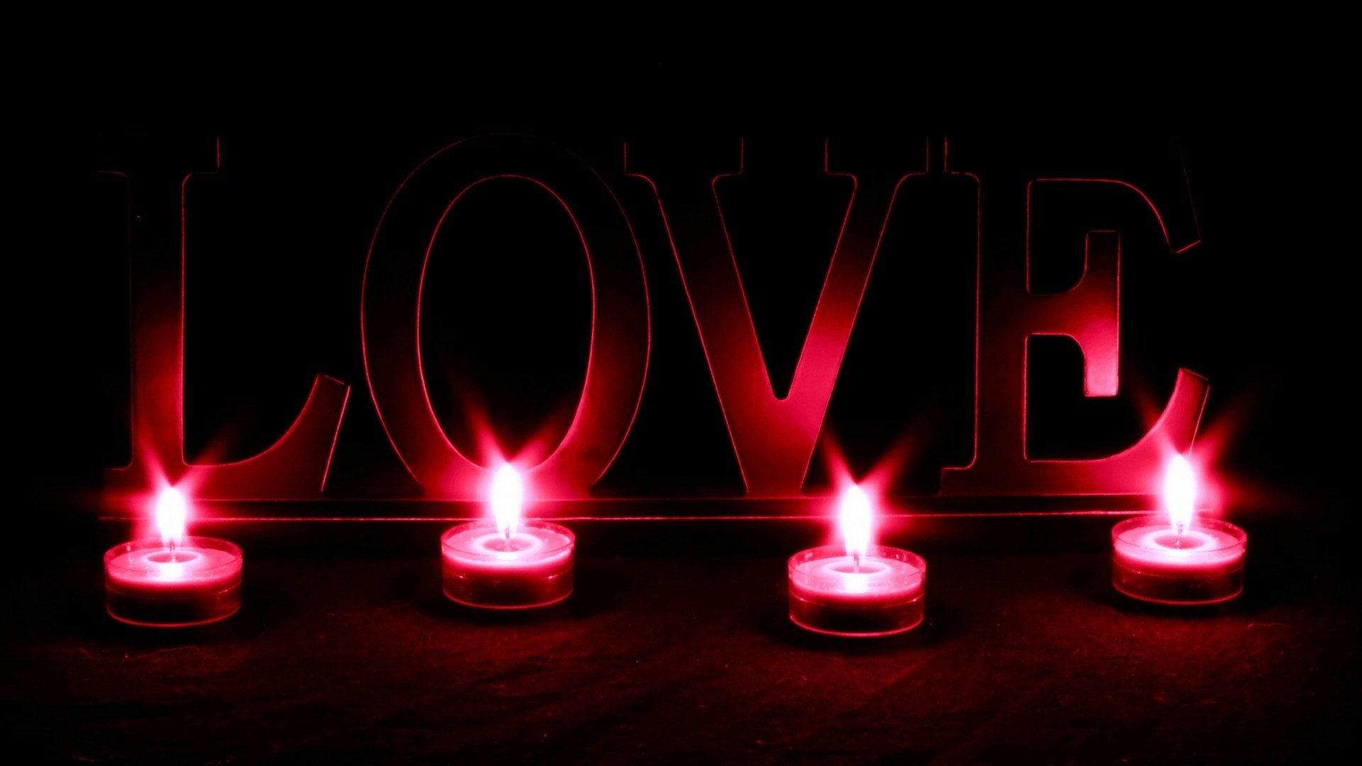 Artistic HD desktop wallpaper featuring the word LOVE illuminated by five glowing red tea light candles against a dark background.