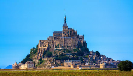 HD PC desktop background: Mont Saint-Michel, a religious abbey and medieval village rising from tidal flats beneath a clear blue sky.