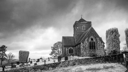 Black and white image of the Church of St Martha-on-the-Hill in Surrey, England, set against a cloudy sky with surrounding gravestones.