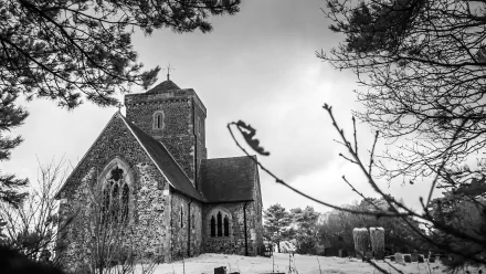 Black-and-white 2K Quad HD PC wallpaper: Church of St Martha-on-the-Hill, a historic religious stone church in Surrey, England, amid snow-dusted graves and bare trees under a moody sky.