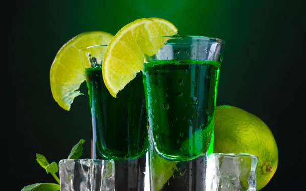 Close-up of two green cocktails with lime wedges on ice, captured in stunning 8K Ultra HD for PC desktop wallpaper and background.